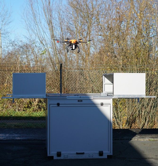 UAV Drohne startet aus automatisiertem Drohnen Hangar mit Ausfahrmechanismus auf Asphaltfläche im