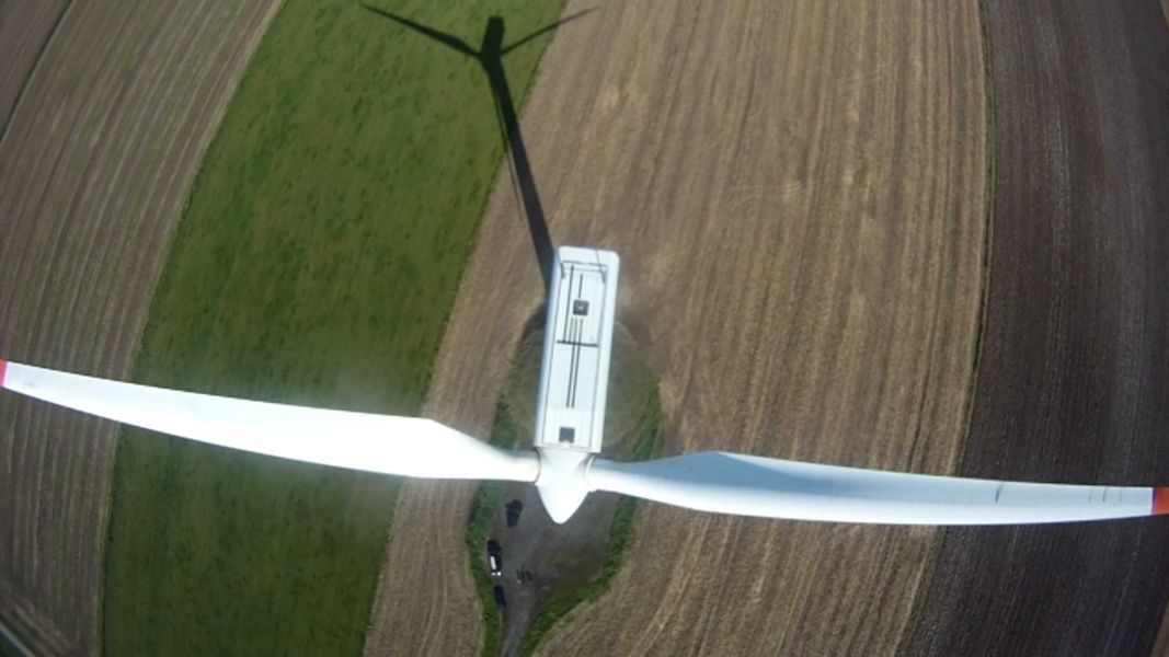 Drohnenaufnahme von oben auf eine Windkraftanlage mit langen Rotorblättern über einem Feld.