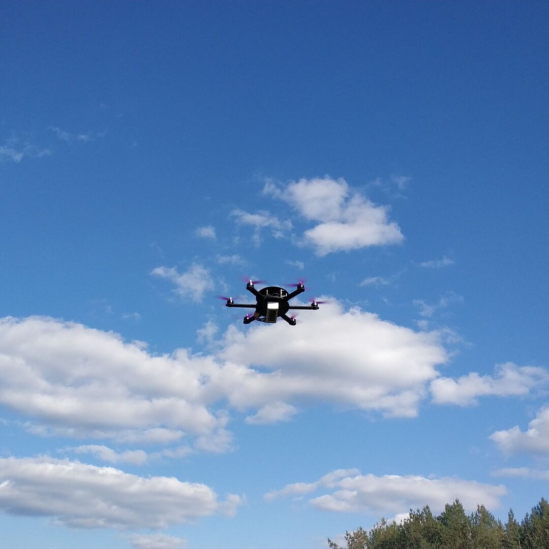 Kompakte UAV Drohne im Flug vor blauem Himmel mit weißen Wolken über bewaldeter Landschaft. Ideal für Tests Flugszenarien und mobile Einsätze.