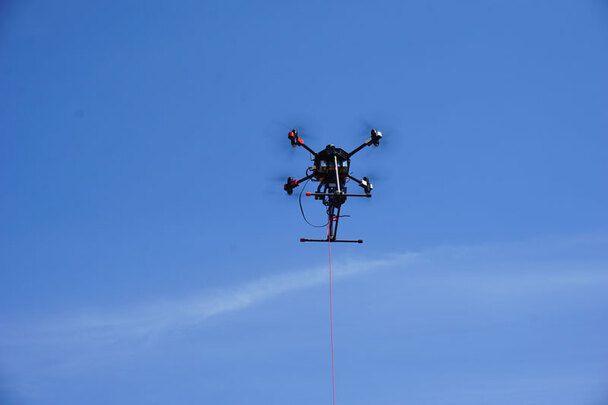 Gefesselte Drohne  im stabilen Schwebeflug bei blauem Himmel. Ideal für Langzeiteinsätze sichere Datenverbindung und stationäre Überwachung.