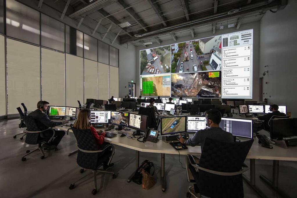 Leitstelle mit mehreren Operatoren vor Monitoren und großer Bildschirmwand zur Steuerung und Überwachung von Drohneneinsätzen über GCS Software