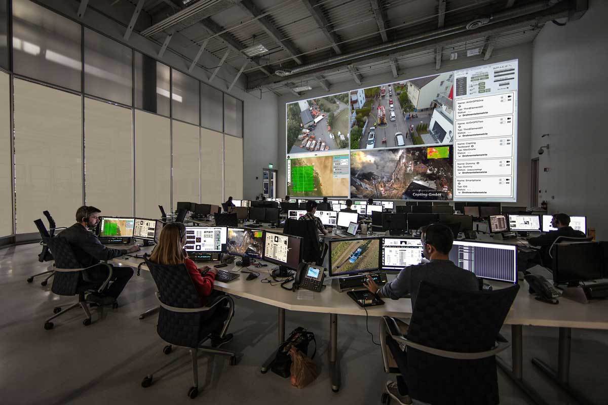 Leitstelle mit mehreren Operatoren vor Monitoren und großer Bildschirmwand zur Steuerung und Überwachung von Drohneneinsätzen über GCS Software