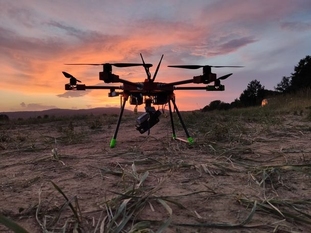 Industrie-Drohne mit Kamera und Landegestell auf trockenem Feld bei Sonnenuntergang. Beratung, Tethering, Systemintegration europaweit.