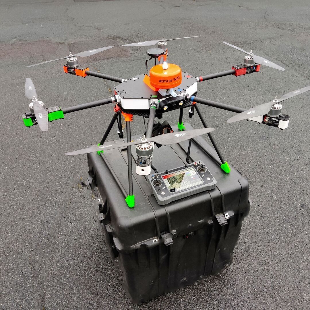 Industrial drone with control unit placed on transport case standing on asphalt. Suitable for mobile UAV missions tethering and system integration.