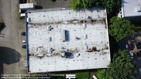 Aerial view of a flat roof with bright and dark areas, surrounded by trees and street.