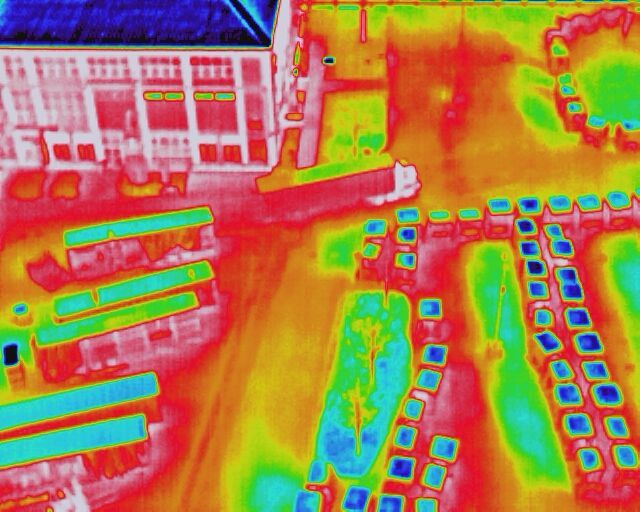 Thermal image of an area with parking lots, paths, and buildings in various temperature colors.
