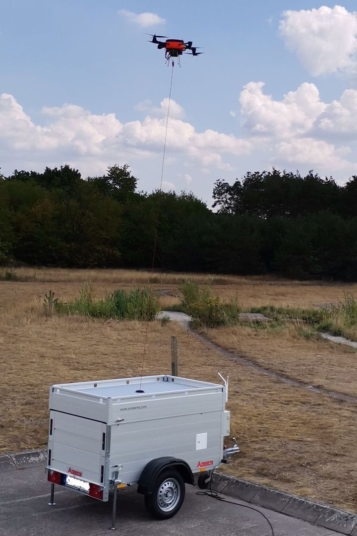 Tethered drone in flight connected to mobile ground station on trailer in dry landscape